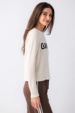 Z SUPPLY Varsity Stand In Sweater in Sandstone, cream knit pullover with navy logo lettering, worn by model with brown track pants, side view.