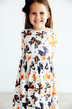 Mila Trick Or Twirl 3/4 Sleeve Pocket Twirl Dress in Halloween bow print worn by smiling girl with black hair bow