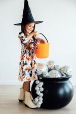 Mila Trick Or Twirl 3/4 Sleeve Pocket Twirl Dress in Halloween print worn by girl in witch hat with orange candy bucket