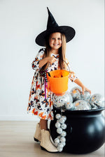 Mila Trick Or Twirl 3/4 Sleeve Pocket Twirl Dress in Halloween print worn by girl with witch hat and orange candy bucket