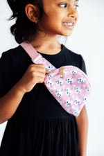 Mila Unicorn Kitties Belt Bag in pink with cartoon cat faces, worn crossbody by a smiling young girl in a black dress.