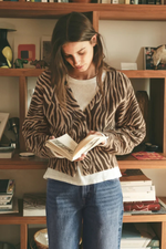 Z SUPPLY All The Wild Cardigan in dark chocolate zebra print worn by model over white tee with blue jeans, reading a book.