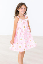 Young girl wearing pink Mila & Rose ruffle cross back dress with rainbow and gold dot pattern in You Are My Sunshine colorway