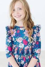 Mila Vintage Garden Ruffle Twirl Dress in teal floral print with ruffled shoulders, worn by young girl model, front view.
