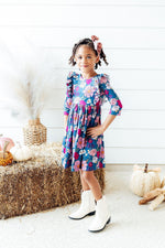 Mila Vintage Garden Ruffle Twirl Dress in teal floral print with pink blooms, ruffle shoulders, worn by young girl with white cowboy boots