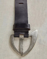 Free People Wtf Noa Belt in black — dark leather strap with aged silver asymmetric shield-shaped buckle, flat lay close-up