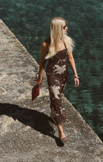 Z SUPPLY Charisma Floral Midi Dress in dark chocolate brown with cream leaf print, worn by model on coastal stone walkway