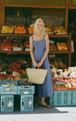 Z SUPPLY Leonora Indigo Midi Dress in Classic Indigo worn by model at a Spanish fruit market, holding a straw tote bag.