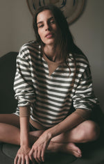 Z SUPPLY Low Key Stripe Sweatshirt in Monstera, olive and cream horizontal stripes, worn by model seated cross-legged, front view