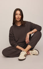 Z SUPPLY Uptown Jogger in Cocoa Bean worn by model seated cross-legged, paired with cream sneakers, front view