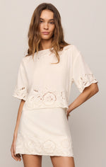 Z SUPPLY Daya Embroidered Top in white worn by model, featuring eyelet floral embroidery, short sleeves, and scalloped hem over matching mini skirt.