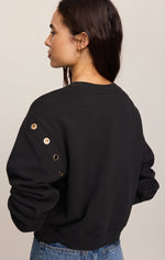 Z SUPPLY Axel Grommet Sweatshirt in black, back view on model, showing gold grommet details along left shoulder seam, worn with jeans.