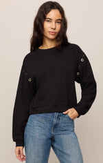 Z SUPPLY Axel Grommet Sweatshirt in black, front view on model, featuring gold grommet details along shoulder seams, crew neck, and relaxed fit with blue jeans.