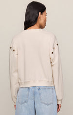 Z SUPPLY Axel Grommet Sweatshirt in Sandstone, back view on model, cream fleece with gold grommets along sleeves, paired with light wash jeans.
