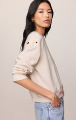 Z SUPPLY Axel Grommet Sweatshirt in Sandstone, side view on model, cream fleece with gold grommet shoulder detail and blue jeans