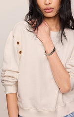 Z SUPPLY Axel Grommet Sweatshirt in Sandstone, model wearing cream pullover with gold grommet details on shoulder sleeve