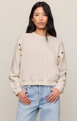 Z SUPPLY Axel Grommet Sweatshirt in Sandstone, front view on model with light jeans, featuring gold grommet details along sleeves.