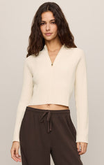 Z SUPPLY Summit Half Zip Sweater in Sandstone — cream ribbed knit crop top with gold zipper, worn by model with dark trousers, front view.