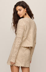 Z SUPPLY Cressa Cardigan in Natural — model wearing back view of beige eyelet lace cropped cardigan with scalloped hem and matching mini skirt