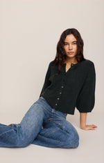 Z SUPPLY Valor Cardigan in Emerald Cove dark green, button-front with puff sleeves, worn by model seated in blue jeans