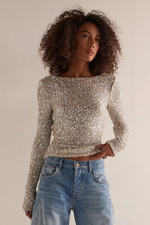 Free People Leading The Way LS silver sequin long-sleeve crop top with boat neckline, worn by model with blue jeans, front view.
