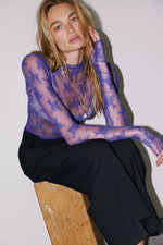 Free People Lady Lux Layering Top in Blue Beam — sheer purple-blue lace long-sleeve top worn by model seated on wood block