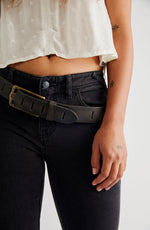 Free People WTF Jona Belt in black leather with gold brass buckle and slot details, worn over dark wash jeans