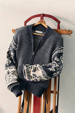 Free People WTF Isle Tide Zip-Up in charcoal, a Nordic-pattern knit sweater with half-zip, displayed on a wooden sled hanger