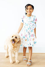 Mila Puppy Pals Belt Bag worn by young girl in matching dog-print dress, round white bag with bow detail, lifestyle photo with goldendoodle