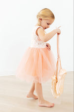 Young girl wearing Mila Ballet Tank Tutu Dress in soft blush pink with sequined bodice and tulle skirt, holding ballet shoes