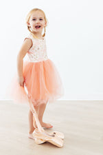 Young girl wearing Mila Ballet Tank Tutu Dress in blush pink with floral bodice and flowing tulle skirt, holding ballet shoes