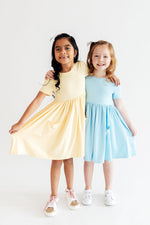 Mila & Rose S/S Pocket Twirl Dress in Butter Yellow worn by girl with friend in blue dress, showing short sleeves and full skirt