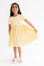 Young girl wearing Mila & Rose S/S Pocket Twirl Dress in soft butter yellow, short sleeves, gathered skirt with pockets