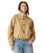 Steve Madden Fayden Jacket in tan/khaki with stand collar, dark buttons, and elasticated hem, worn by model with wide-leg jeans.