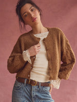Free People Thistle Cardi in Macadamia, a warm camel bouclé cropped cardigan with gold buttons, worn open over a lace-trimmed white top with jeans.