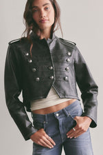 Free People Ryland Vegan Band Jacket in black, cropped military-style with silver double-breasted buttons and epaulettes, worn by model with jeans.