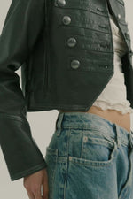 Free People Ryland Vegan Band Jacket in black with silver snap buttons, worn over white top with blue jeans, close-up torso view.