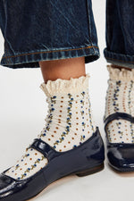 Free People Rosebud Waffle Knit Ankle socks in ivory with floral print and ruffled lace cuff, worn with navy patent loafers and cuffed denim.