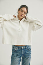 Free People Celeste Quarterzip in Clean Ivory, cropped ribbed half-zip pullover with brass zipper, worn by model with blue jeans, front view.