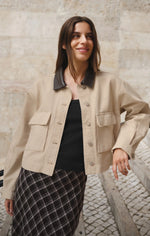 Z SUPPLY Rey Cropped Chore Jacket in Soapstone beige with dark leather collar, cargo pockets, worn by model over black top and plaid skirt