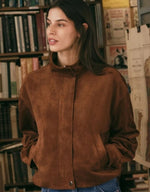 Z SUPPLY Corin Bubble Hem Jacket in Saddle Suede brown, model wearing relaxed suede jacket with mock neck and snap closure in bookstore setting